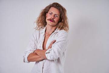 Curly longhaired man applying with pink lipstick at his lips and wearing creative look posing - obrazy, fototapety, plakaty