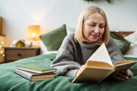 Mature woman reading book on bed at home. Christmas time, the magic of the holiday.