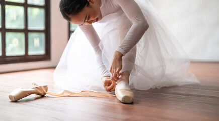 Ballerina in ballet shoes. Asian girl tying ribbons of toe shoes. ballet dancer preparing and...