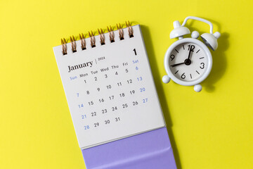January 2024.Desk calendar for 2024 and alarm clock on a lilac background.