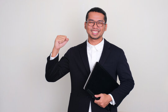 Asian businessman holding a laptop and clenched fist showing optimistic gesture