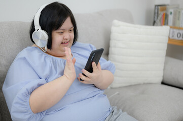 A disabled young woman with Down syndrome uses social media and uses a mobile phone to make video calls in the living room at home.