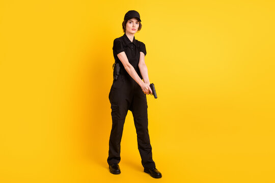 Full size photo of serious policewoman in black uniform go walk with pistol in hands isolated on yellow color background