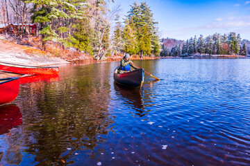 Fototapeta premium young woman paddling a green canoe solo on a river with trees clad in freshly fallen snow in the background room for text shot on the ottawa river in eastern ontario canada 