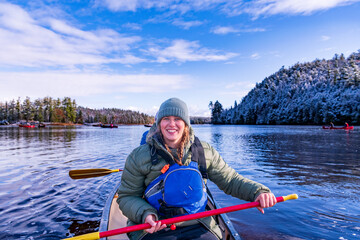 young woman paddling in a green canoeon a river with trees clad in freshly fallen snow in the...