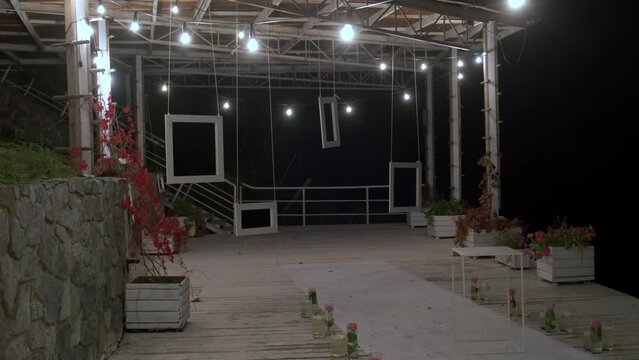 A dockside venue for a nighttime wedding ceremony with lots of lights and mirror paintings hanging from the ceiling, and flowers on the floor.