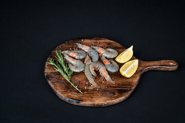 Fresh raw shrimps arranged on a round wooden board with rosemary and pepper ready to cook