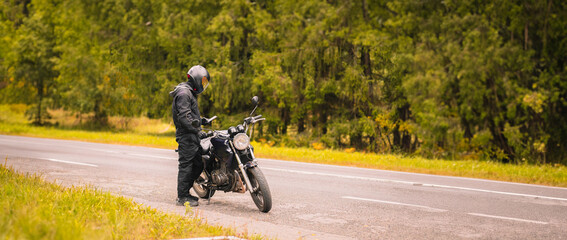 motorcyclist in motorcycle clothing and a helmet on a custom stylish motorcycle on a forest asphalt road