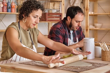 Woman kneading clay with rolling pin in a ceramic workshop. Hobby and craft concept.