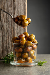 Spicy olives in a glass bowl on a stone table.