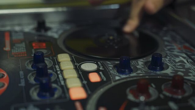 A DJ touches the buttons and sliders of a DJ mixer with his hands, playing electronic music. Close-up