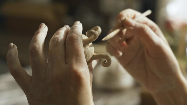 A woman makes a small flower pot from clay and works with a brush. Close-up. Creative hobby.