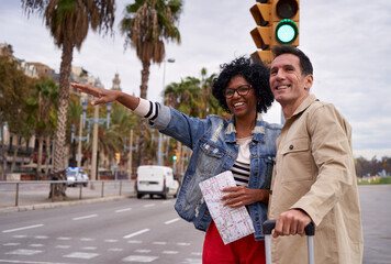 Smiling middle-aged multiracial couple with luggage hailing a taxi in the city street during their holidays. Copy space. - obrazy, fototapety, plakaty