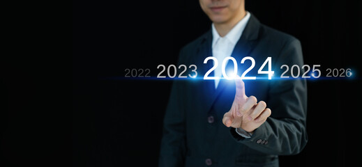 Businessman finger pressing and pointing on year 2024 on virtual screen on dark background....