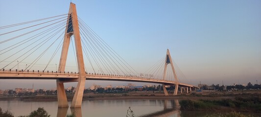 The view of the bridge between the river and trees and the blue sky at sunset