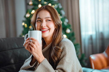 Happy asian woman holding coffee cup sit couch in house indoors with Christmas x-mas atmosphere...