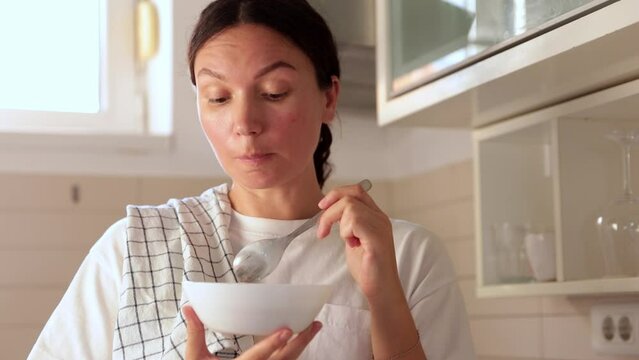 A housewife girl stands in the kitchen and a plate in her hands eats delicious food and enjoys a new recipe