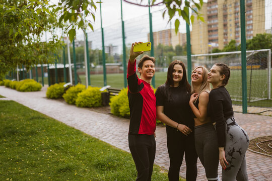 Smiling man holds phone for selfie with sports friends. Entertainment and relaxation after training outdoors. Group photo