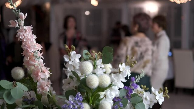 Beautiful holiday bouquet close-up on background of dancing women with blurred focus in restaurant.
