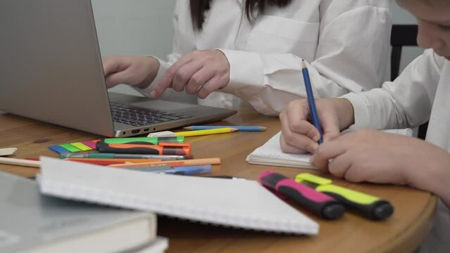 Medium shot of the hands of a boy who draws while his mother is working at a computer, sitting together at a table in the kitchen.