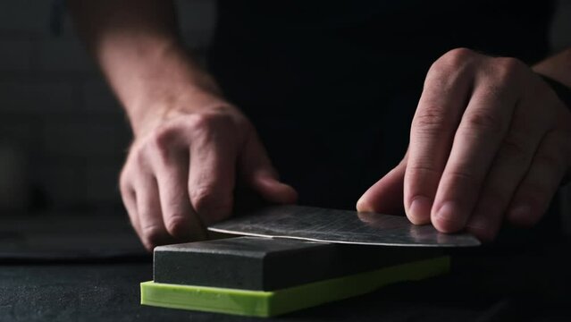 Male Hands Sharpening Kitchen Knife With Water Whetstone On A Kitchen Table, Close Up View