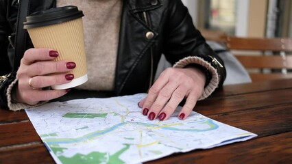 Stylish Female Tourist Checks City Sightseeing Route On Map While Sipping Coffee In Street Cafe
