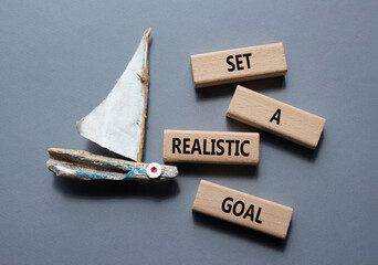 Set a realistic goal symbol. Concept words Set a realistic goal on wooden blocks. Beautiful grey background with boat. Business and Set a realistic goal concept. Copy space. - obrazy, fototapety, plakaty