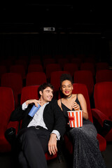 cheerful multiracial couple in black chic attires holding soda and popcorn and smiling happily