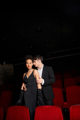 good looking multicultural couple in evening black outfits posing together at cinema while on date