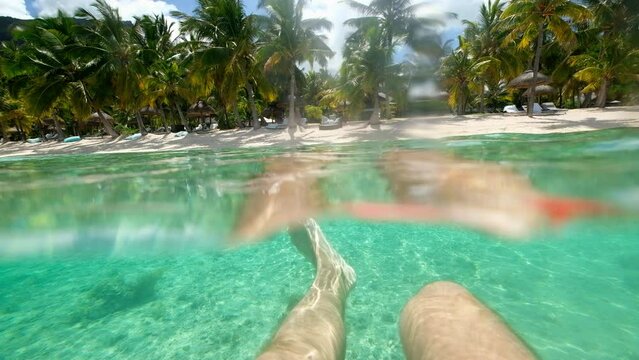 POV video of a man swimming in crystall clean waters of Le Morne lagoon waves at sandy beach with exotic luxury resort sun beds, umbrellas. Tropical vacations and traveling concept 4K footage.