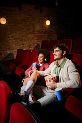 cheerful diverse stylish couple in retro attires smiling and watching movies on date in cinema
