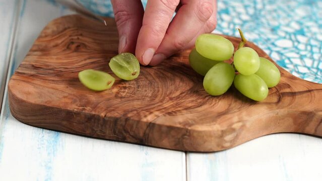 Green grapes without seeds are cut into quarts on a wooden board made of olive wood.