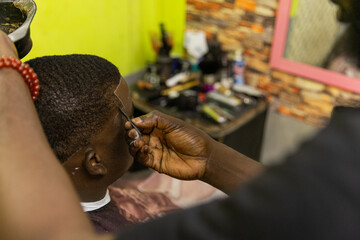 An African barber applies hair dye to his customer in the barbershop