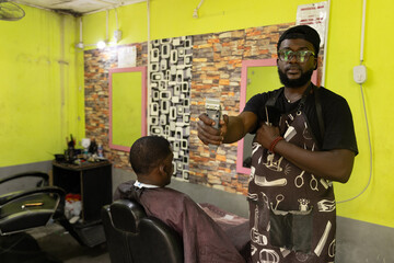 A barber in his barbershop holds a razor while his customer looks at himself in the mirror