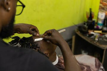 A barber defines the edge of his client's hair during a haircut with the straight razor - obrazy, fototapety, plakaty