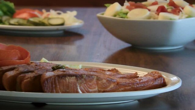 Mão colocando azeite com alcaparras em salmão grelhado com salada ao fundo desfocado. Comida saudável.