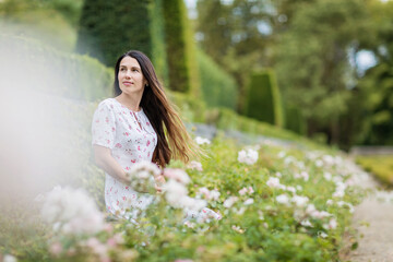 Portrait of young attractive woman sitting among white roses in picturesque old park of small town near an ancient French castle