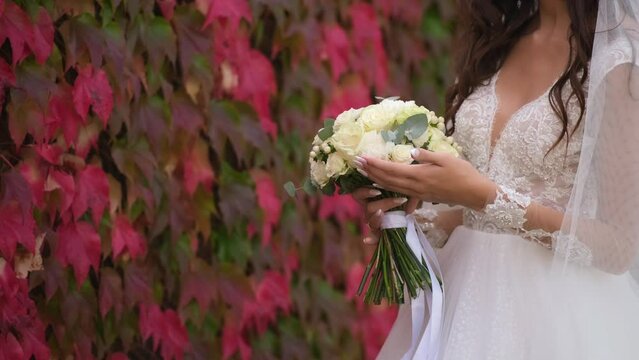 Close-up of a bouquet of roses in the hands of the bride against the red ivy on the wall on a fall afternoon.
