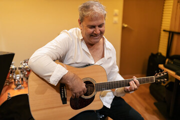 Obraz premium Positive mature man playing acoustic guitar in studio