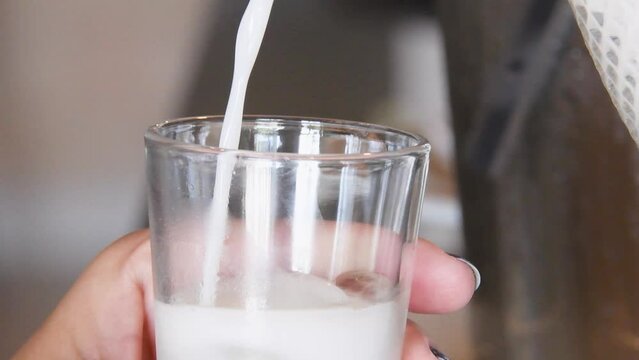 M&atilde;os femininas servindo bebida branca em copo pequeno