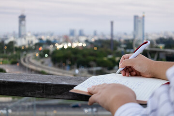 A close up of a woman writing in a notebook with a pen on sunset downtown with skyscrapers...