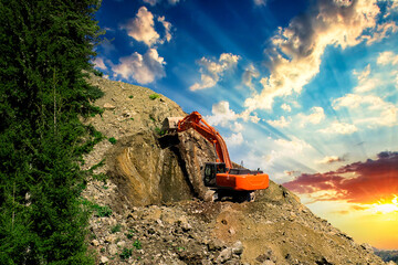 Excavator at a construction site on the side of a hill against a cloudy blue sky. Compact...