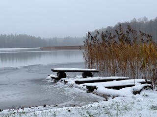 pokryta śniegiem kładka wędkarska na jeziorze przy trzcinach 