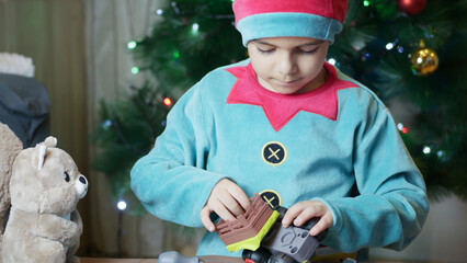 Cute boy elf assembling toys for kids in front of Christmas tree. High quality photo