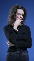 Thoughtful woman thinking deeply about decision with hand on chin in blue background. Caucasian...