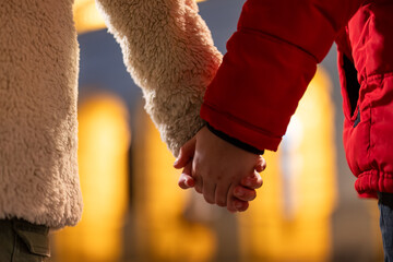 Rear view photo of boy and girl holding hands while walking. Focus is on the hands. Two...