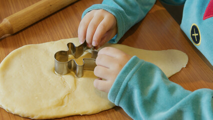 Adorable boy dressed as an elf using cookie cutters to cut gingerbread man dough. Christmas tree in...