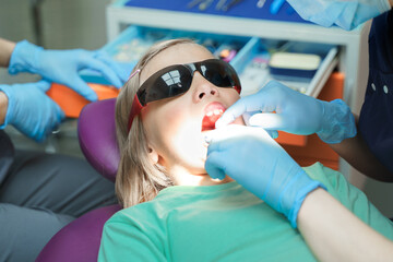 Little scared girl sitting in chair in dentist doctor office. Protective safety sunglasses....