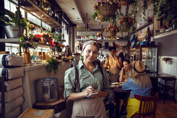 Portrait of a confident mature waitress standing in small local restaurant