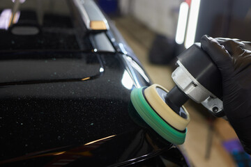 Man with an orbital polisher in car workshop polishing car closeup